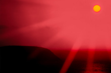 Morning Hawaii sunrise with a yellow sun and red beaming sky over a hillside next to the ocean with light reflecting off of the Pacific Ocean,の写真素材