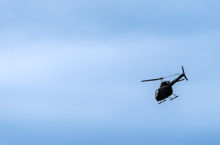 Single helicopter flying at an angle silhouetted against a blue sky with wispy cloudsの写真素材
