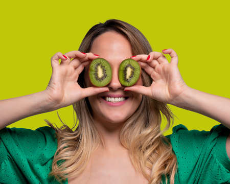 Happy and smiling young man playing with an orange cut in half and in front of his eyes. Photo on solid color backgroundの写真素材