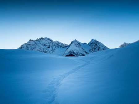 A path leads to the fresh snow with the peak of the Piz Pisoc in the distance ,Engadine, Switzerlandの写真素材