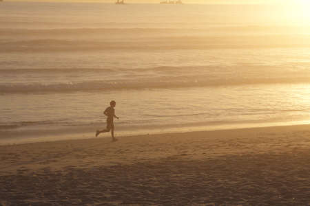 Jogger jogging on the beach at sunset with orange backgroundの写真素材