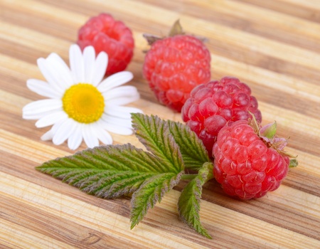 Fresh Ripe Raspberries with Leaf and White Camomile Flower on Old Wooden Hardboardの写真素材
