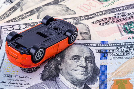 Close-up crushed red car toy on dollar bill background. Concept of car insuranceの写真素材