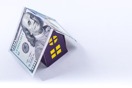 hundred dollar bill roof covers purple cardboard house with yellow windows isolated on white background.Concept of a good investmentの写真素材