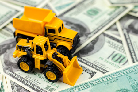 Construction vehicles for building concept. Yellow toys truck, backhoe on dollar bills background.の写真素材