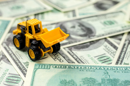 RUSSIA, ST.PETERSBURG - February 03, 2018: Construction vehicles for building concept. Yellow toy backhoe on dollar bills background.の写真素材