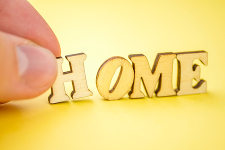 The concept of a phased construction of a private house or apartment. The accumulation of money for real estate. A man's hand holds the letter "H" with his fingers and brings the letters with the general word "home" on a yellow background.  Close up.の写真素材