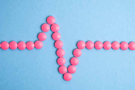 Heart cardiogram made of pink pills on blue background.の写真素材