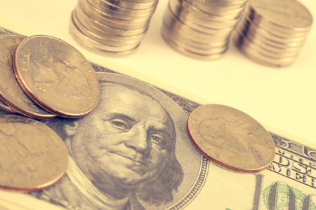 Coins and stacks of coins on a hundred dollar bill on a white background. Toned.の写真素材