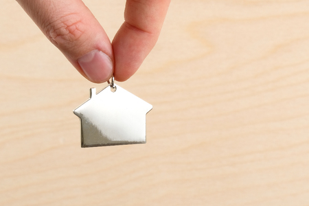 The concept of buying or renting or insuring a home and real estate. Fingers hold a metal figure of the house on the background of the texture of the white house.の写真素材