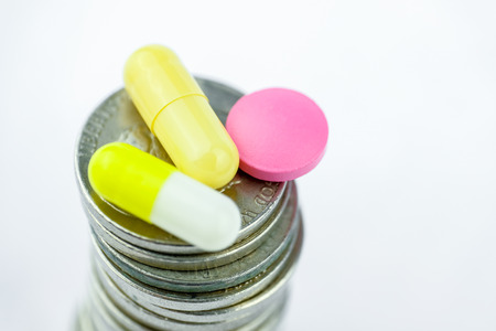 Yellow capsules and a pink pill on a stack of coins on a white background. The concept of business on drugs.の写真素材