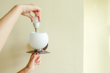 The girl changes the light bulb in the lamp.の写真素材