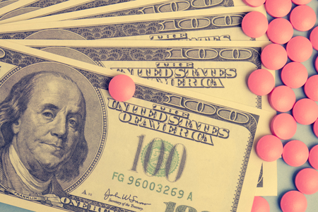 Scattered pink pills lie on one hundred dollar bills on a blue background. The concept of expensive drugs or the high cost of health. Toned.の写真素材