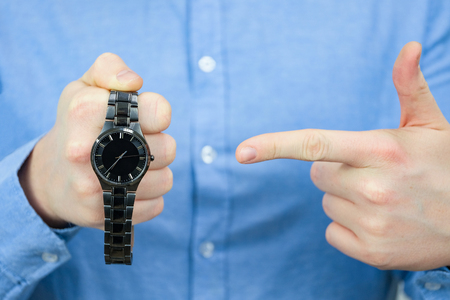 Time management concept. A man in a blue shirt holds a black watch and points his finger at them.の写真素材