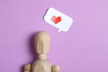 Wooden doll with a red heart made of paper in balloon on a purple background