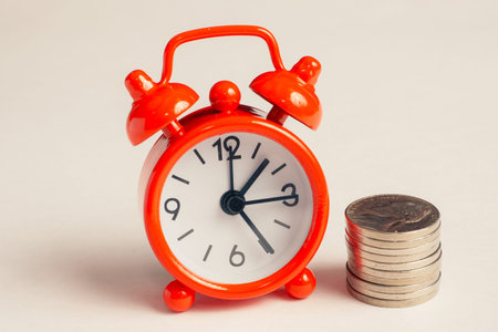 Classic red clock next to a stack of coins. Toned.の写真素材