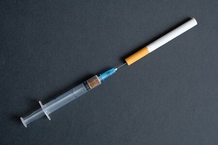 Smoking is a bad habit and harm to health. Comparison with hard drugs. Syringe with tobacco and a cigarette on a black background.の写真素材
