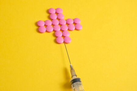 Cross of pink pills on a yellow background with a syringe. The concept of the required number of drugs.の写真素材