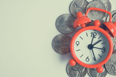 Red vintage clock on coins on right side. Place for text. Time saving money. Top view.Toned.