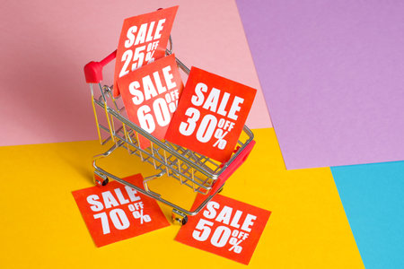 Online shopping discount concept. Red labels with percents in trolley on a multicolored background.の写真素材