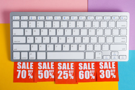 Online shopping discount concept. Red labels with percents under the white keyboard on a multicolored background.の写真素材