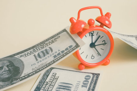 Concept time for financial gain. Red vintage clock with one hundred US dollar bills on a yellow...