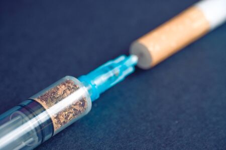 Smoking is a bad habit and harm to health. Comparison with hard drugs. Syringe with tobacco and a cigarette on a black background. Toned; Close up.の写真素材