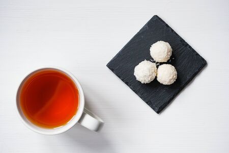 White coconut candy balls in plate shale dishes on rustic wooden background with a cup of tea. Top view.の写真素材