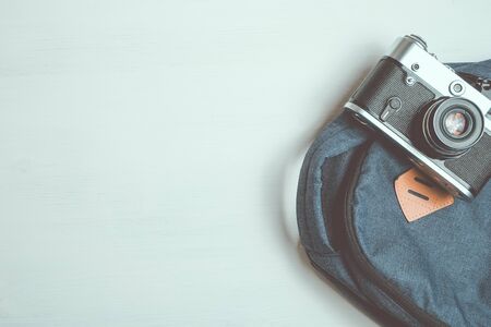 Retro camera lies on a fashionable backpack on a white wooden background. Copy space. Toned.の写真素材