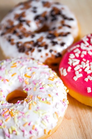 Pink, white and brown glazed donuts on wooden background. Close up. Vertical.の写真素材