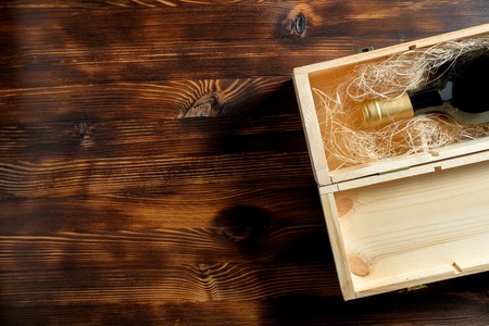 A dark expensive bottle of wine in a wooden box on a wooden background. Top view with copy space. Close up.の写真素材