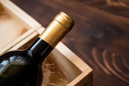 A dark expensive bottle of wine in a wooden box on a wooden background. Close up.の写真素材