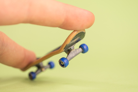 Fingerboard. Man make trick by two fingers with small skateboard on green background. Close up.の写真素材