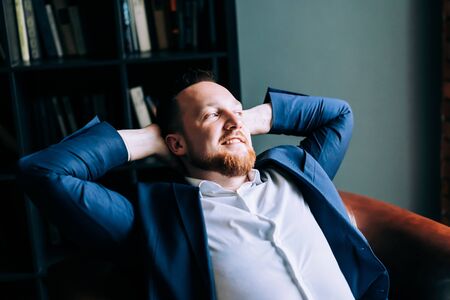 Adult successful businessman in a suit sits in a chair and feels success.の写真素材