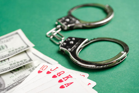 Handcuffs lie next to playing cards and US dollars on a green background. Gambling crime concept....