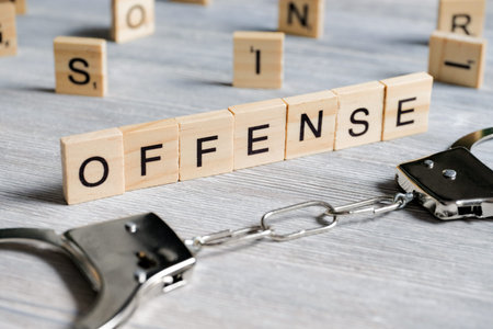 A word made of wooden letters is an offense. Metal handcuffs on a gray background. The concept of...
