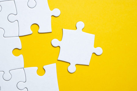 Final white piece is lying next to the jigsaw puzzle on yellow background. Concept of support,...