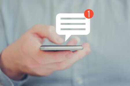 A man in a shirt holds a smartphone with his hand. Abstract notification message icon. Social networking concept. Close up.の写真素材