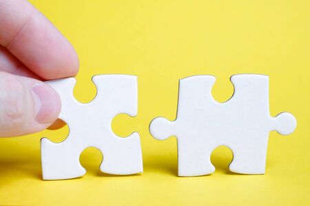 The concept of the full picture after the last detail. A piece of the puzzle is held by the fingers of a man next to another on a yellow background. Close up.の写真素材