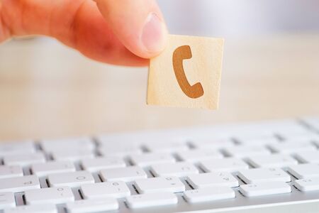A man holds a wooden cube with the image of a telephone symbol in his hand. Contact concept for communication. Close up.の写真素材