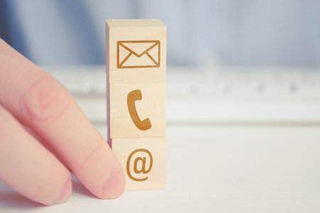 A man holds a wooden cube with the image of a phone, email, letters symbol. The concept of contacts...