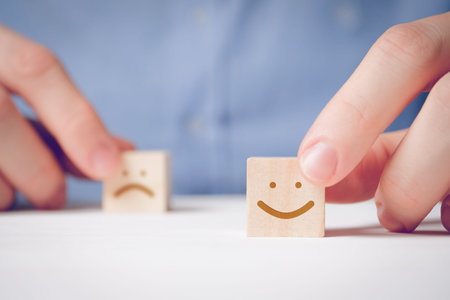 A man holds with his fingers a wooden cube with a positive face next to a disgruntled one. Concept...