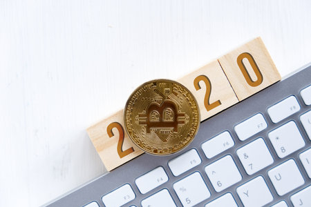 Bitcoin with numbers 2020 on wooden cubes on a white keyboard with a wooden background. Flat lay....