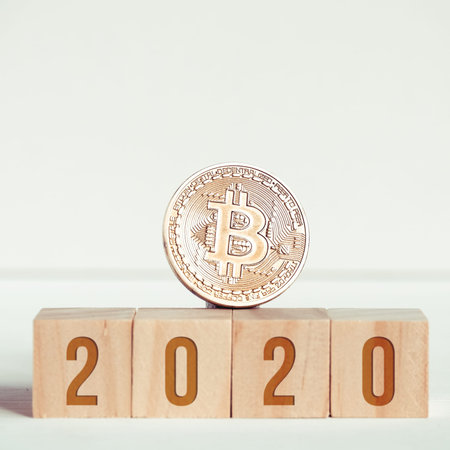 2020 numbers on wooden cubes on a white background next to a bitcoin coin. The concept of...
