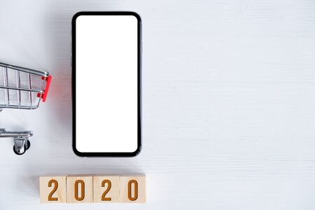 Figures 2020 on cubes and a white wooden background with a trolley. Smartphone with mock up. The concept of sales and purchases. Flat lay. Close up.の写真素材