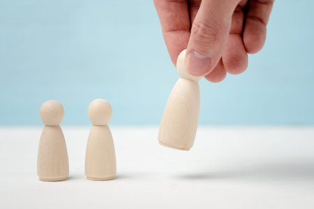 Two small wooden figures are looking how male hand puts or removes big figure on blue background.