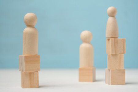 Three abstract wooden figures of people stand on different levels are made of toy blocks on blue...