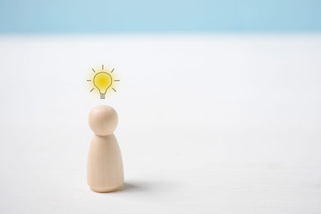Concept of idea generation by man. Wooden figurine with a burning light bulb above it. Close up.の写真素材