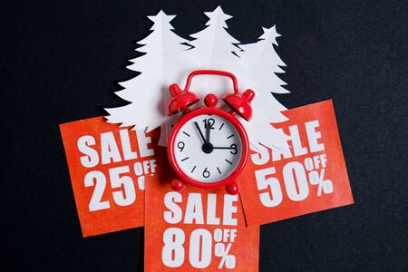 Christmas trees made of white paper on red plates with discounts and a vintage watch on a whatman paper in black. Christmas sale concept. Flat lay, close up.の写真素材