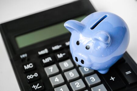 Close up of blue piggy bank on calculator on white background. The concept of saving.の写真素材